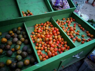 kinds of tomato and rotten oranges on the green rack shelf that sells in the traditional market with dark background, selective blurred focus