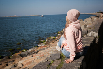 a blonde girl on the background of a cold sea, seagulls in the sky. travel and travel concept, immigration. girl pouring at the beach, casual outfit, backpacker, traveler