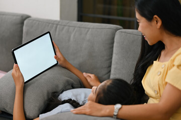 Mom and her child looking on digital tablet during her daughter laying on mom's lap, Empty screen of tablet, Happy family are spending time together, Mother's day concept.