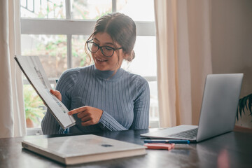 One young pretty woman studying and doing homework at home on the table. Female teenager using laptop or computer surfing the net indoor.