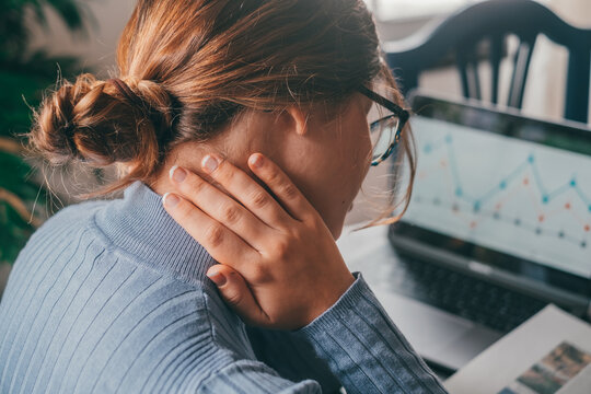 One young woman feeling bad and having pain for overstudying at home on the table. Neck ache concept. Portrait and close up of hands touching neck.