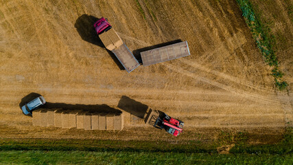 Agricultural tractor loads wheat straw briket on truck. Aerial view. Agricultural machinery © vladdeep