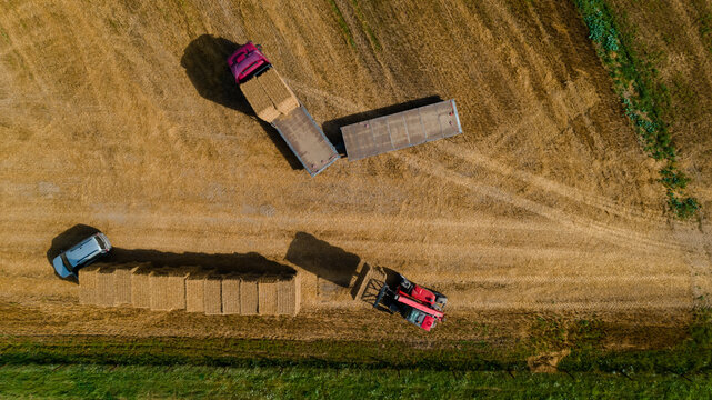 Agricultural tractor loads wheat straw briket on truck. Aerial view. Agricultural machinery