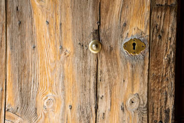 old natural wood door with brass knob and lock, weathered bare wood. Authentic vintage front door. 