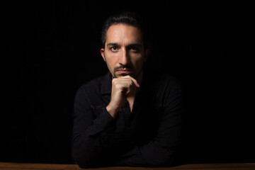 Business photo of a man in a black shirt sitting at a table. Male portrait on a black background.