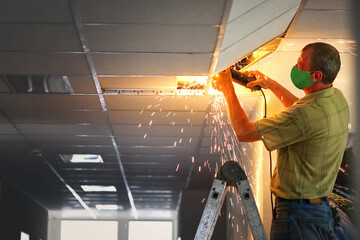 Unrecognizable worker on ladder work with angle grinder, sawing metal. Man repairing ceiling lighting. electrician worker sawing