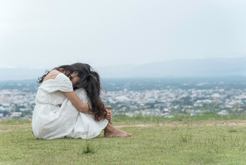 woman sit facing side face down knee on grass at top mountian sky ,city and nature view background....
