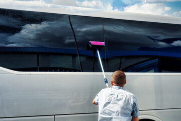 Driver brushes large tinted windows of bus on summer day. Care and maintenance of equipment....