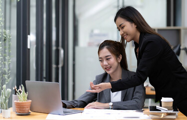 Two young Asian business woman talk, consult, discuss working with new startup project idea presentation analyze plan marketing and investment in the office.