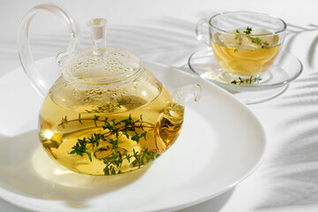 Yellow herbal tea with thyme in glass teapot. White background with copyspace.