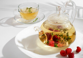Yellow herbal tea with thyme in glass teapot. White background with copyspace.