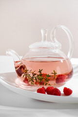 Red herbal berry tea with thyme and fresh raspberry in glass teapot. White background with copyspace.