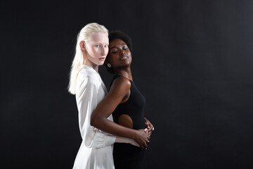 Caucasian albino girl and african american young woman hugging on black background. Women...