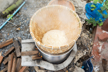 Obraz na płótnie Canvas Sticky rice cooked in wicker bamboo steamer with laos aluminum steel pot on the charcoal stove in the agricultural garden house area.