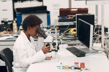 Fototapeta na wymiar Scientist african american woman working in laboratory with electronic tech instruments and microscope. Research and development of electronic devices by color black woman.