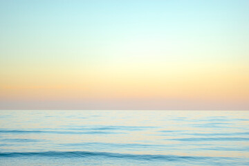 Fototapeta premium Serene and tranquil background of waves at the beach with a tropical yellow orange and gold sunset by the sea