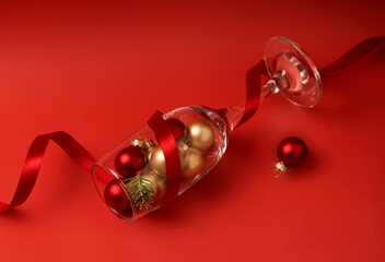 Gold and red Christmas balls in a wine glass decorated with red silk ribbon on a red background....