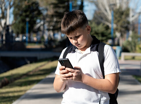 School kid using his mobile in the middle of the street on a sunny day