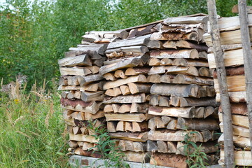 Logs on the grass. Firewood. Birch firewood from hardwoods. Preparation of firewood for the heating season. Natural fuels, firewood for burning in the stove or fireplace