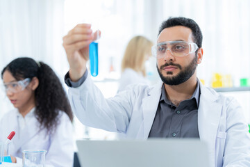 Scientist in lab coat and safety glasses holding test tube with blue solution at modern laboratory. Look at tube and analysis. Research development, bio chemistry, medical and pharmaceutical