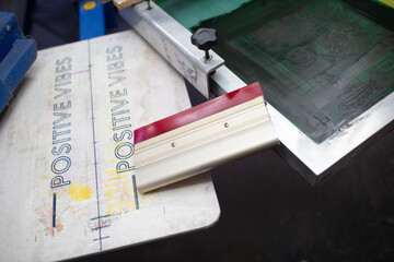 Serigraphy silk screen print process at clothes factory. Frame, squeegee and plastisol color paints.