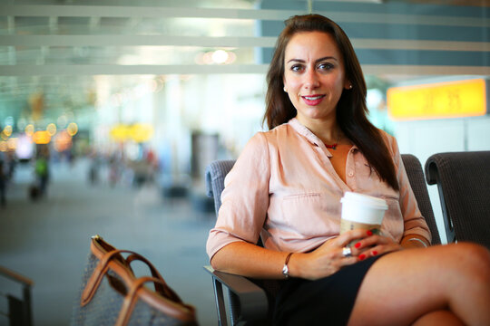 Woman Sitting And Smiling With A Coffee In The Waiting Room Of The Airport