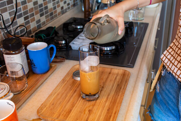 Fototapeta na wymiar A woman hand preparing a glass of cold coffee on a wooden cutting board at kitchen