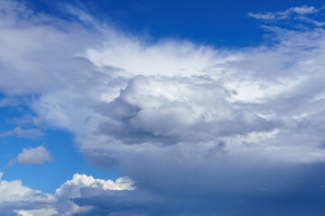 Fluffy white cloud in clear blue sky on sunny day in front of dark low storm cloud