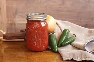 Homemade canned salsa in glass jar on rustic wood background with peppers onions tomatoes - obrazy, fototapety, plakaty