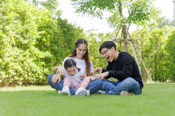 Fototapeta premium Asian Family with a child playing on a lawn, Family sitting on the grass with her happy and adorable little daughter, enjoyment relaxing recreational concept.