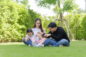 Naklejka premium Asian Family with a child playing on a lawn, Family sitting on the grass with her happy and adorable little daughter, enjoyment relaxing recreational concept.