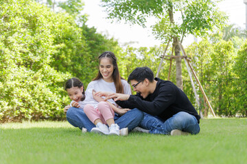 Asian Family with a child playing on a lawn, Family sitting on the grass with her happy and adorable little daughter, enjoyment relaxing recreational concept.