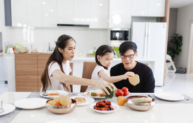 Asian family having meals together and showing thumbs up at home happily, Happy young parents are having fun with their little daughter during lunch at the dining table.