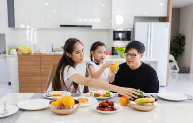 Asian family having meals together and showing thumbs up at home happily, Happy young parents are having fun with their little daughter during lunch at the dining table.