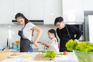 Naklejka premium Asian family couple, husband and child help his to put on apron before cooking in the kitchen at home, happy father and son concept.
