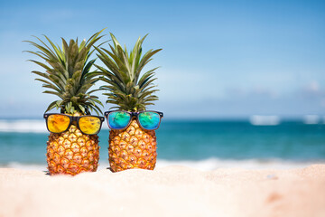 Pineapples in stylish sunglasses on the sand against sea