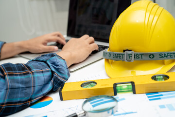 Asian engineer with architectural house plan project blueprint, graph and yellow helmet and engineering construction tools.