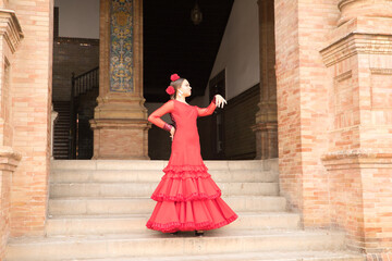 Young teenage woman in red dance suit with ruffles and red carnations in her hair doing flamenco...