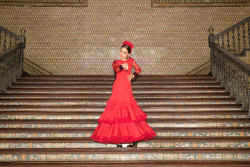 Young teenage woman in red dance suit with ruffles and red carnations in her hair dancing flamenco...