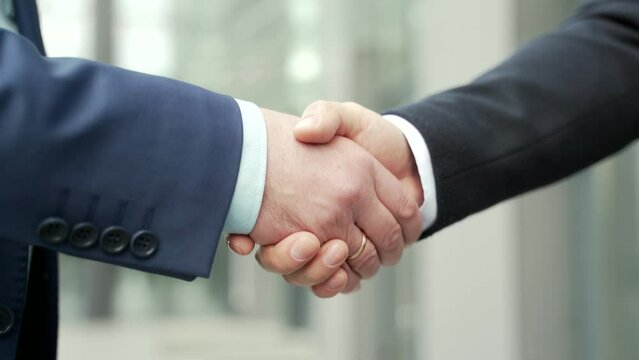 Close up business people shaking hands partnership deal while standing outside on the street near a big office building urban street. handshake closeup outdoor mature asian businessmen in formal suits