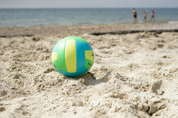 Volleyball ball in blue and yellow colors on a sandy beach near the sea.