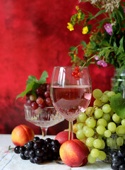 Glass of pink wine, grapes, berries and flowers on a table. Delicious summer food close up photo. Textured background with copy space.