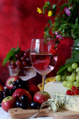 Wine, cheese, fruit and flowers on a table. Vibrant colors of fresh berries and grapes. Colorful still life with glass of pink wine, red and white grapes, gorgonzola cheese and red currant. 
