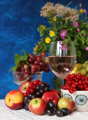 Glass of pink wine, grapes, berries and flowers on a table. Delicious summer food close up photo. Textured background with copy space.