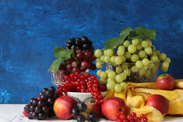 Colorful still life with seasonal berries on a table. Red currant, green grapes, nectarines and apples close up photo. Nutrition concept. 