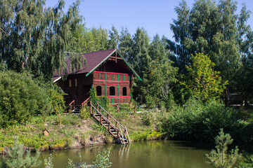 Wooden Russian hut on the shore of a pond with a reflection on a sunny summer bright day in Suzdal russia