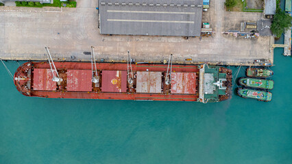 Aerial view from drone of commercial ship with cranes while unloading containers to large commercial ship in the wharf. Transportation and travel background, beautiful sea in summer.
