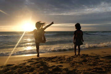 Fototapeta premium Cute Asian sisters playing on the beach during summer vacation at sunset together. Summer family trip to the beach. travel and vacation concept.