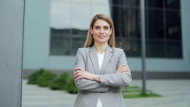 portrait attractive happy business woman employee looking at camera smiling. Caucasian female blonde middle-aged worker stand a city street near urban office center outside outdoor proud arms crossed