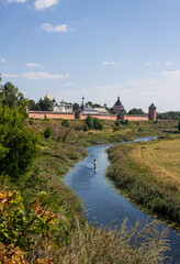 Panoramic view of the old brick walls of the Suzdal Kremlin on a high hill on the banks of the beautiful Kamenka river among the green grass on a sunny summer day in Russia